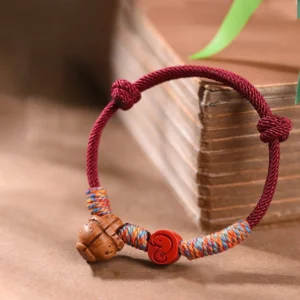 Chinese zodiac red string peach pit cinnabar luck bracelet front view with ancient books and botanical setting