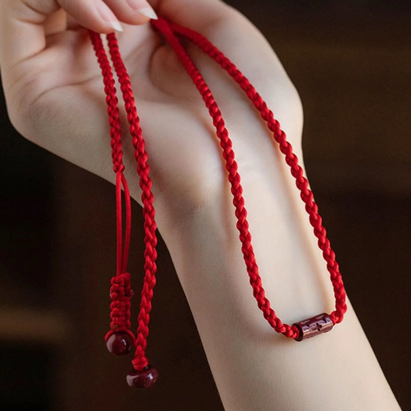 Hand-held braided red string belly chain with cinnabar bead ends and metal accent bead on dark background
