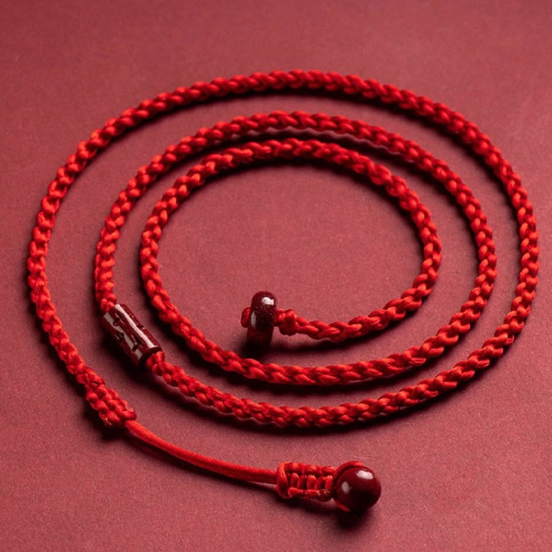 Top-down flat lay of cinnabar belly chain with coiled braided cord, cinnabar bead clasp and metal accent on crimson background