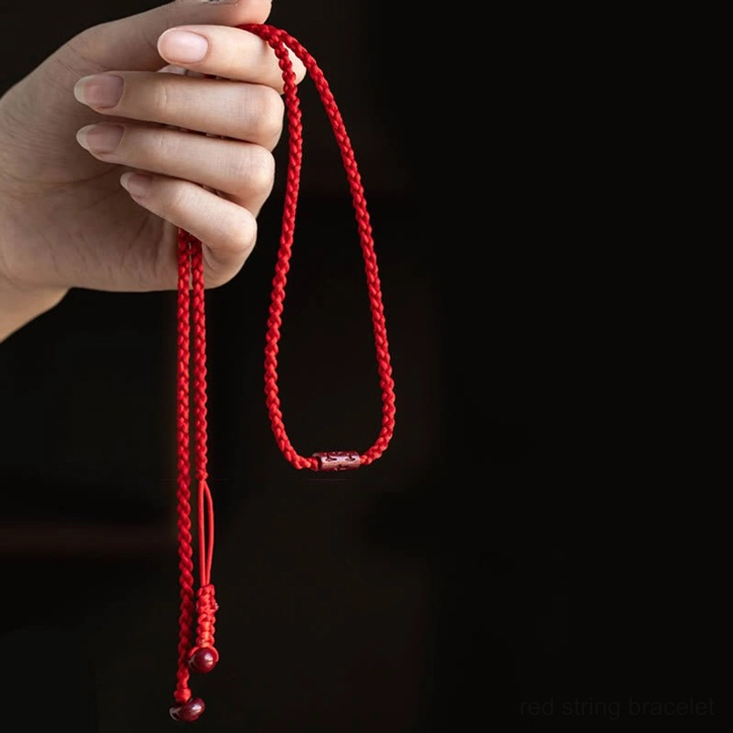Hand-held close-up of braided red string belly chain with cinnabar bead ends showing adjustable length feature