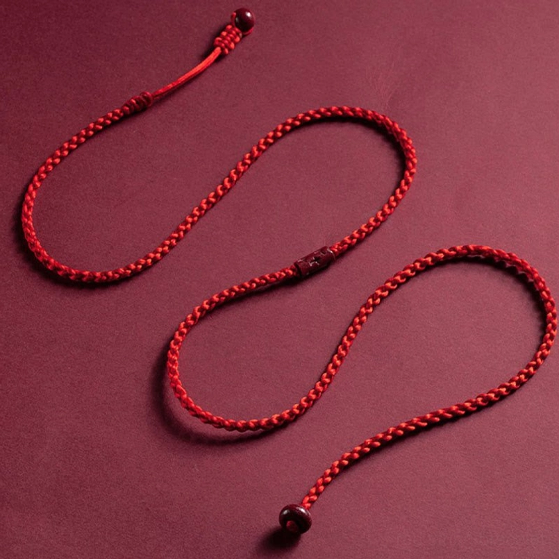 Two coiled braided red string belly chains with cinnabar bead ends displayed on maroon background