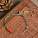 Handmade cinnabar blessing braided bracelet with blue-yellow woven rope, enamel lock charm, and adjustable tassel with red bead on wooden desk