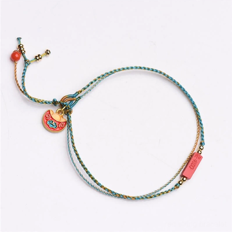 Flat lay top view of handmade double-layer cinnabar blessing bracelet with mixed woven rope, enamel lock charm, and adjustable tassel