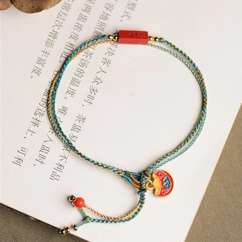 High overhead view of cinnabar blessing braided bracelet on open book page showing complete bracelet design with ji-xiang plaque