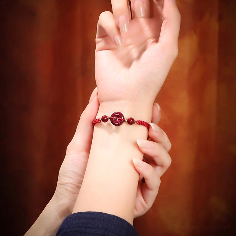 Delicate red cord cinnabar bracelet on wrist with warm fabric background