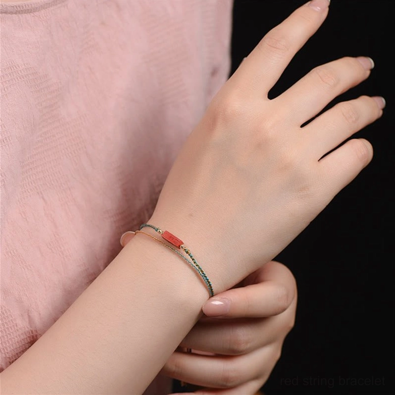 Worn on wrist side-view close-up of slim handmade cinnabar blessing bracelet with thin woven rope and small red cinnabar bar