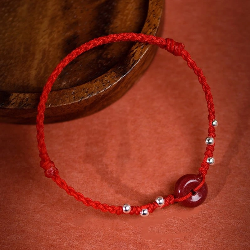 Cinnabar peace buckle bracelet anklet side view on wooden dish with red fabric background