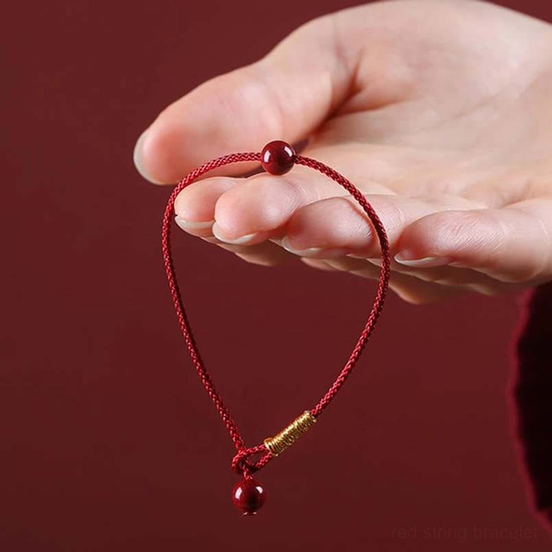Red string cinnabar bracelet close-up with gold wrapped section and hanging bead