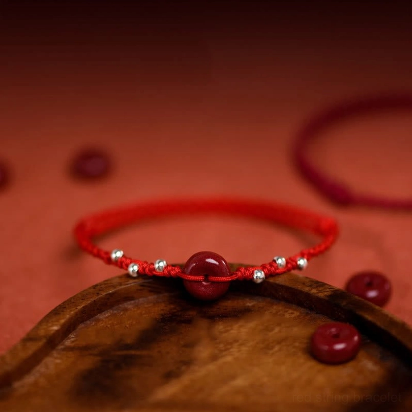 Cinnabar peace buckle red string bracelet low side view on wooden coaster detail shot
