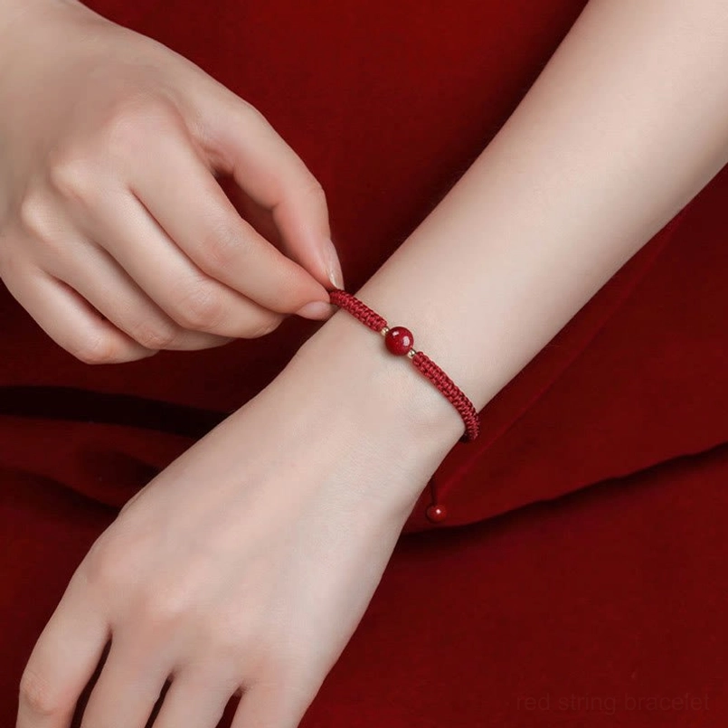 Two hands wearing matching cinnabar red string bracelets showing adjustable sizing