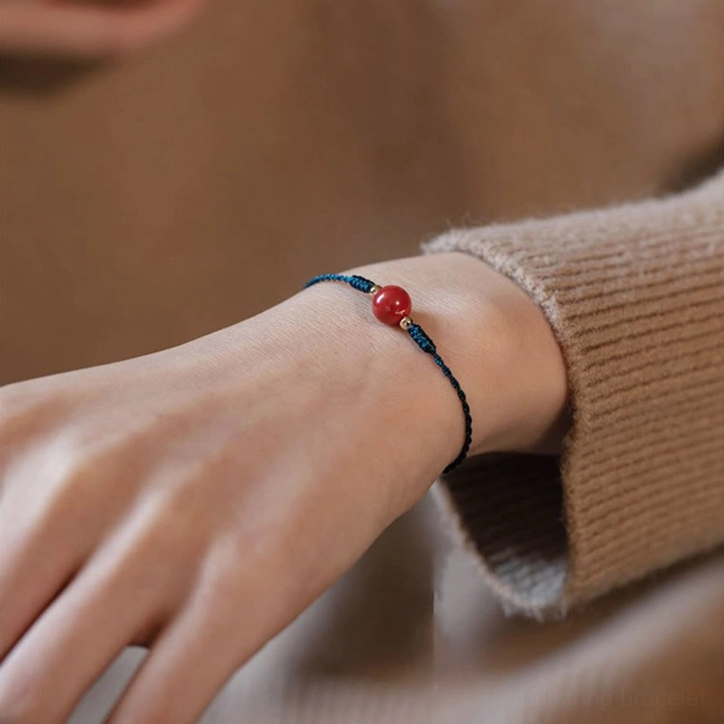 Cinnabar red string bracelet worn on wrist with beige knit sweater