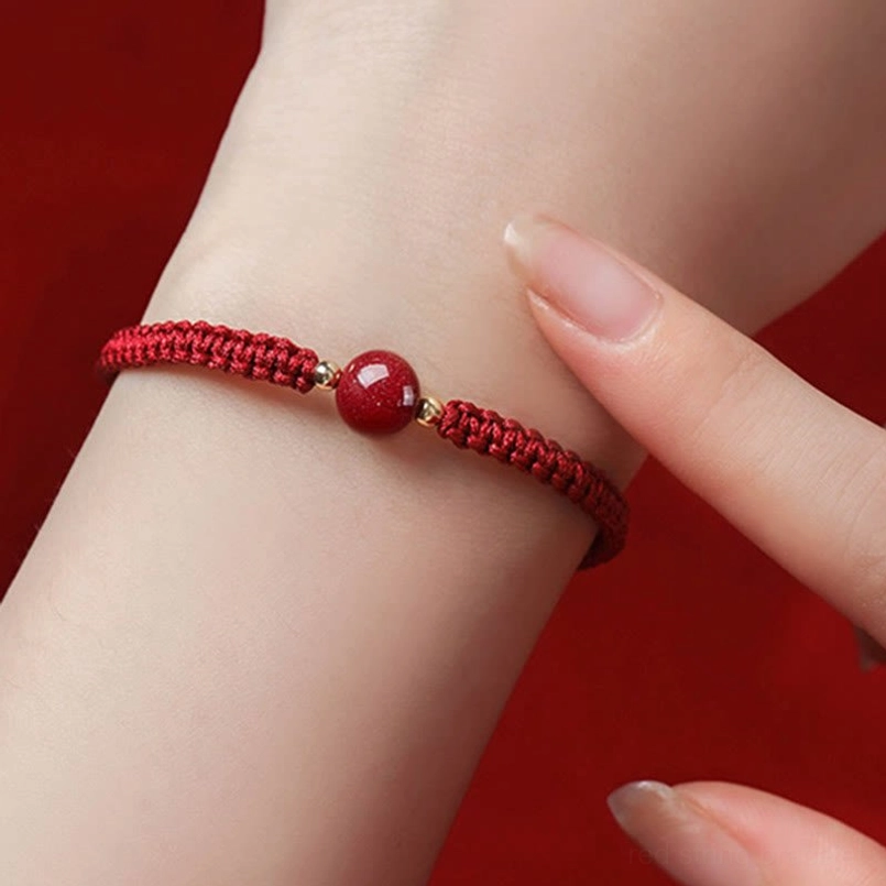 Cinnabar bead bracelet worn on wrist close-up with braided red string design