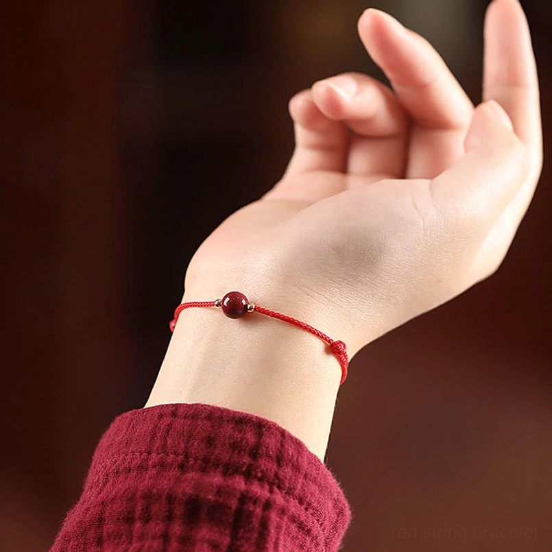 Single cinnabar bead red string bracelet worn on woman's wrist close-up