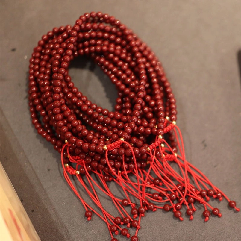 Multiple stacked cinnabar beaded bracelets with red woven tassel ends on dark wood