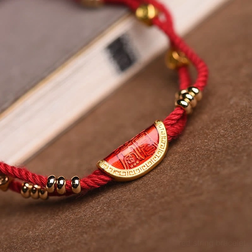 Full flat lay of red string bracelet with gold beads on white studio background