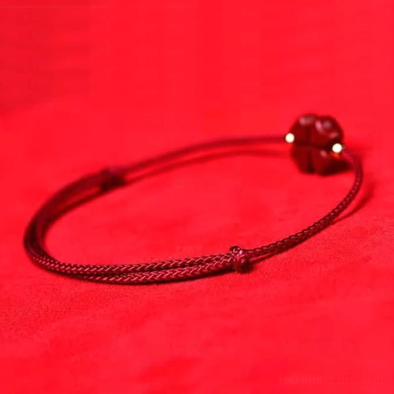 Cinnabar four leaf clover red string bracelet charm detail angled flat lay view