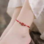 Red cinnabar four leaf clover anklet worn on ankle, daily casual styling with woven red rope and lucky charm