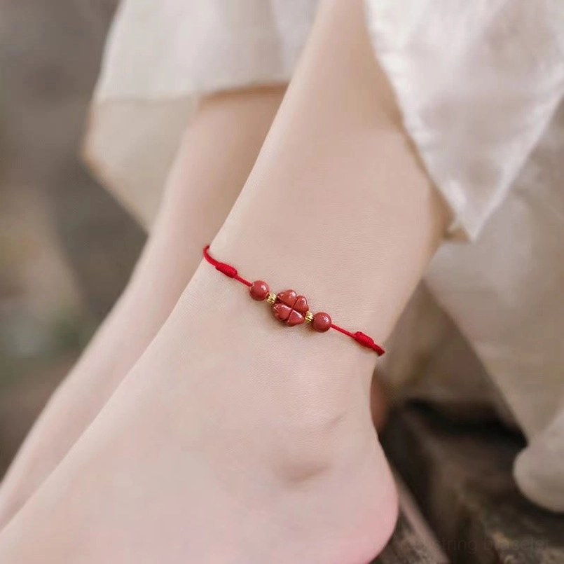 Red cinnabar four leaf clover anklet worn on ankle, daily casual styling with woven red rope and lucky charm