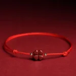 Natural cinnabar four leaf clover red string bracelet flat lay with dark red fabric background