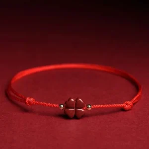 Natural cinnabar four leaf clover red string bracelet flat lay with dark red fabric background