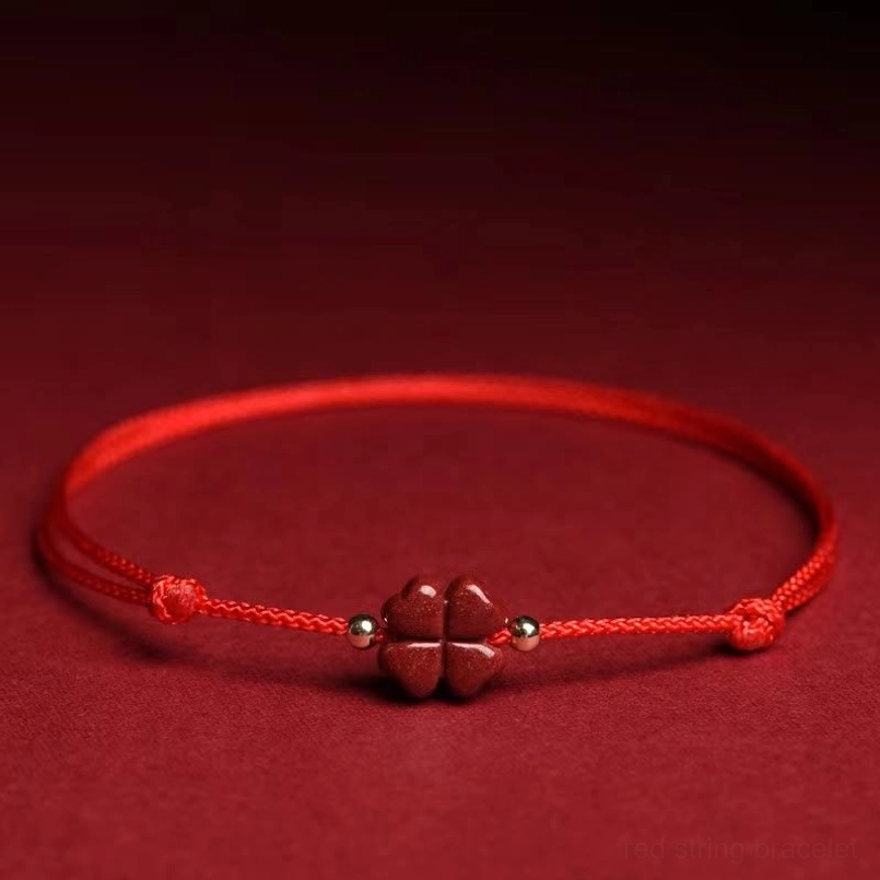 Natural cinnabar four leaf clover red string bracelet flat lay with dark red fabric background