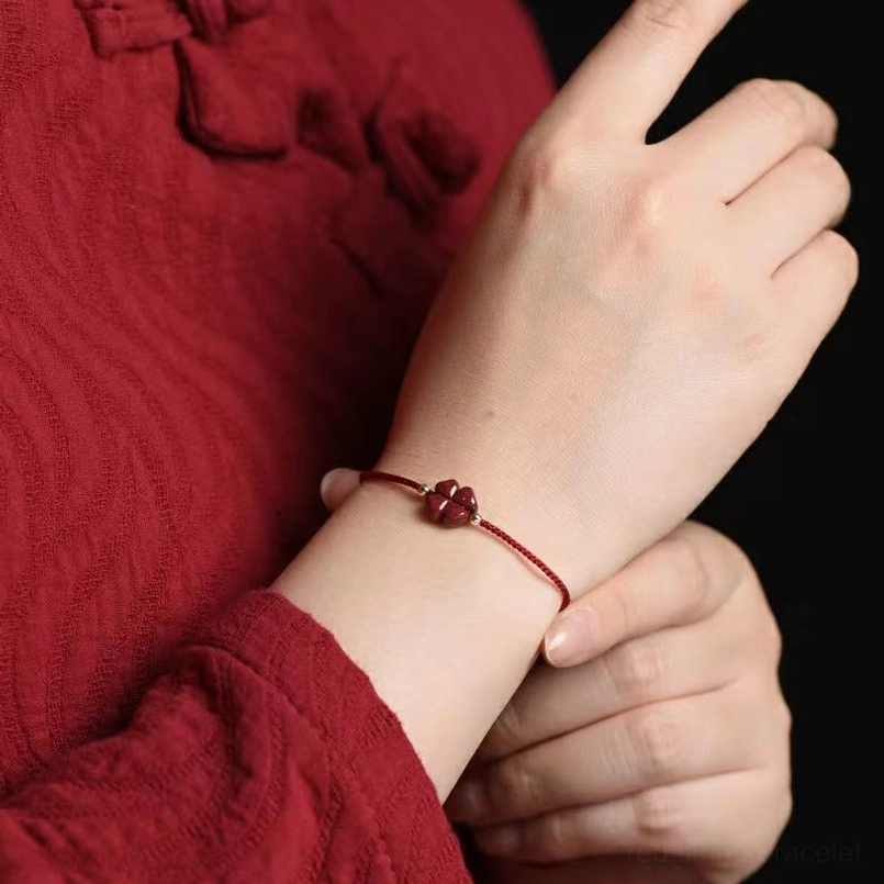 Dark red cinnabar four leaf clover string bracelet worn on wrist close-up side view