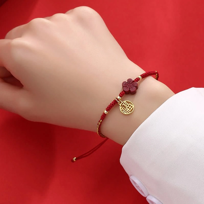 Red and gold woven cinnabar Fu bracelet worn on wrist with white sleeve