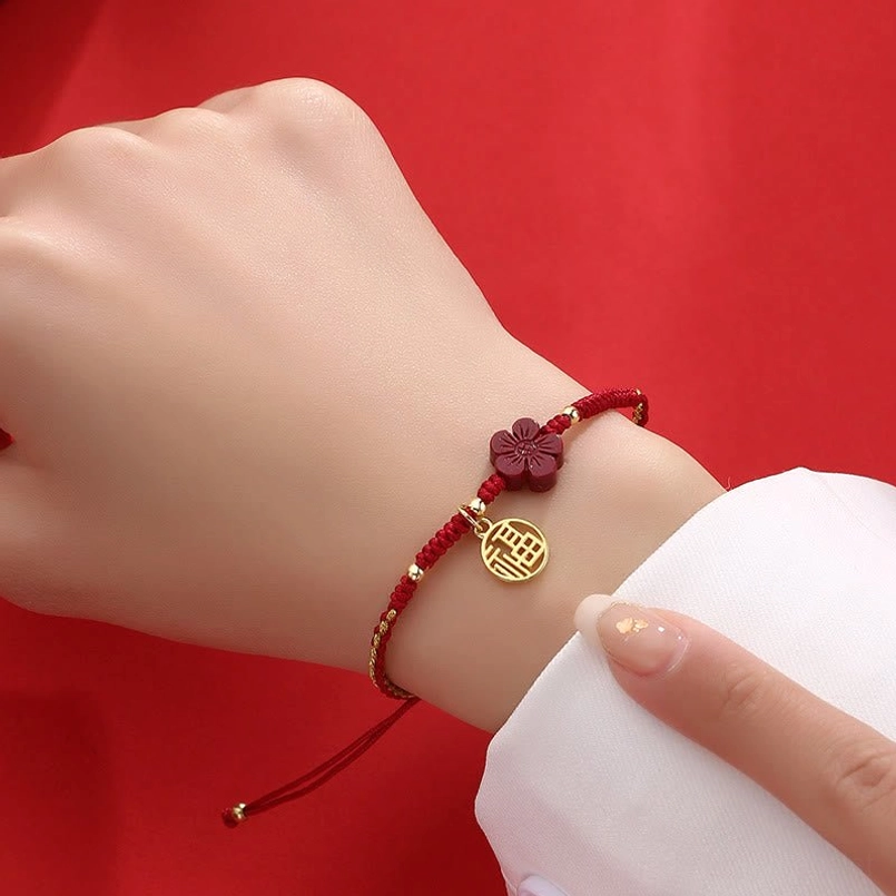 Red string cinnabar bracelet on wrist showing Fu pendant and flower charm detail