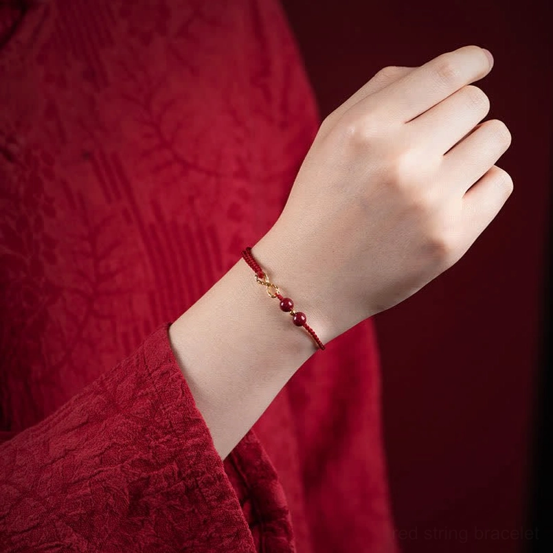 Red string infinity bracelet worn on wrist, side close-up view showcasing gold charm and cinnabar details