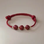 Cinnabar jade lotus red string bracelet with carved beads and gold spacer details - flat lay