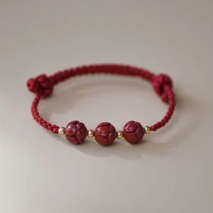 Cinnabar jade lotus red string bracelet with carved beads and gold spacer details - flat lay