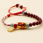 Cinnabar koi fish blessing bracelet flat lay with red string and gold pendant charm