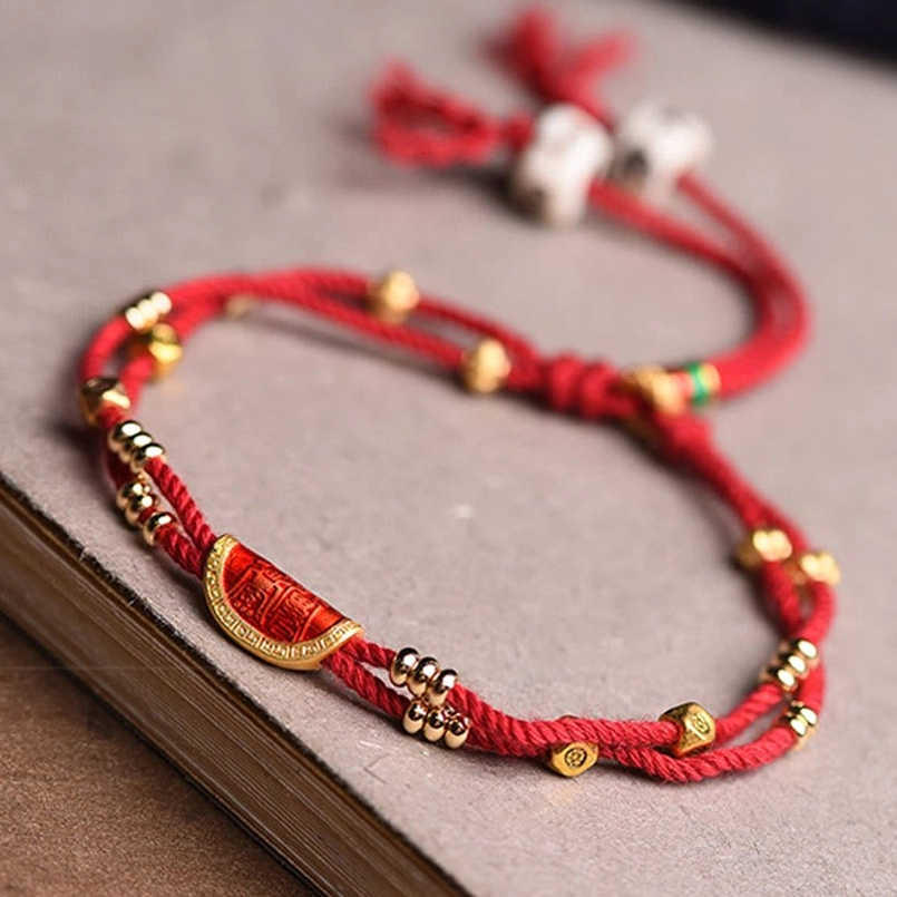 Red rope bracelet with gold beads and crescent charm on wooden book surface