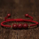 Cinnabar Om Mani Padme Hum engraved blessing bracelet with dark red rope overhead flat lay
