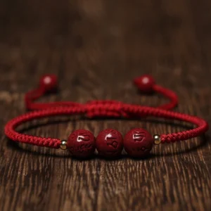 Cinnabar Om Mani Padme Hum engraved blessing bracelet with dark red rope overhead flat lay
