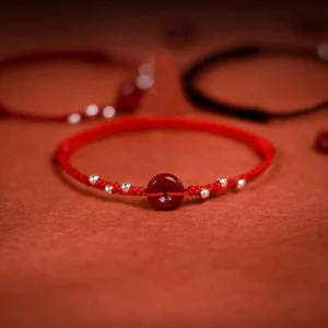 Cinnabar peace buckle red string bracelet overhead flat lay with silver beads on red textile background