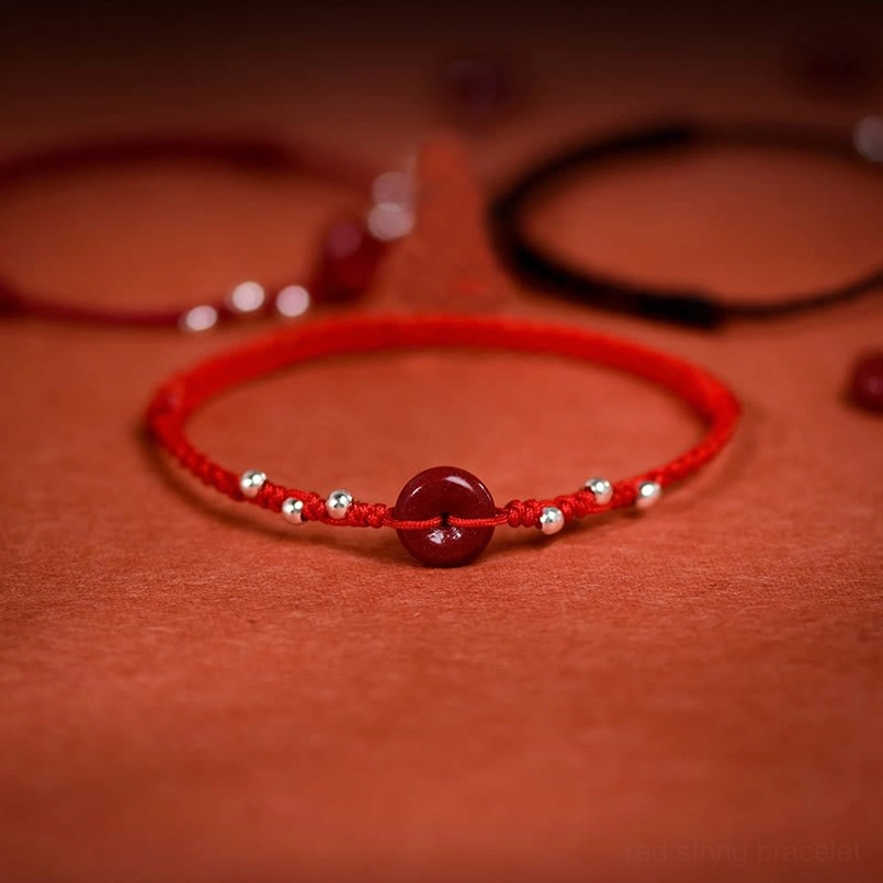 Cinnabar peace buckle red string bracelet overhead flat lay with silver beads on red textile background