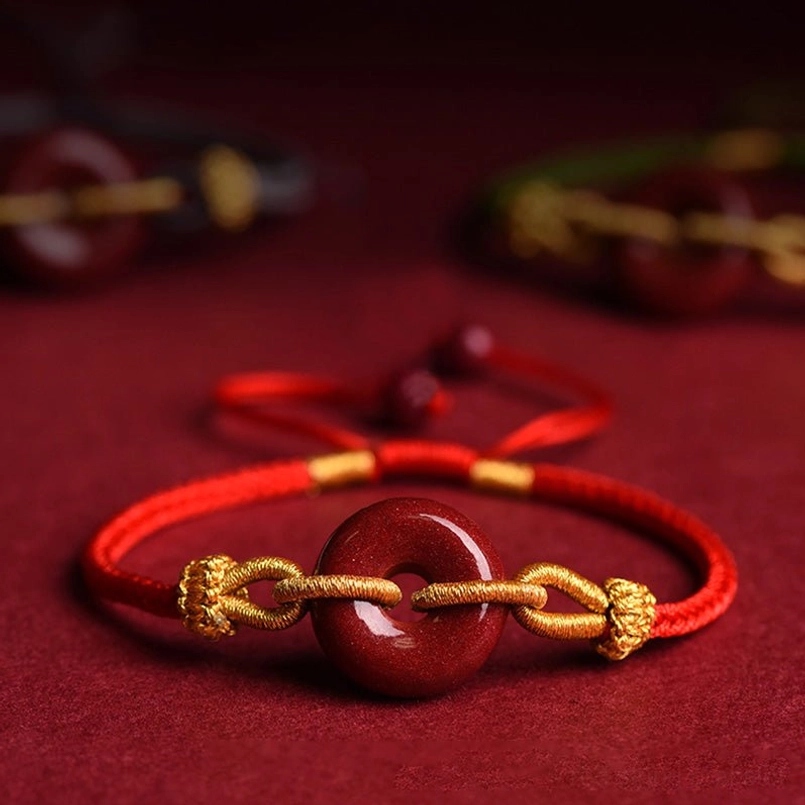 Two matching cinnabar peace buckle bracelets with red rope and gold knot hardware