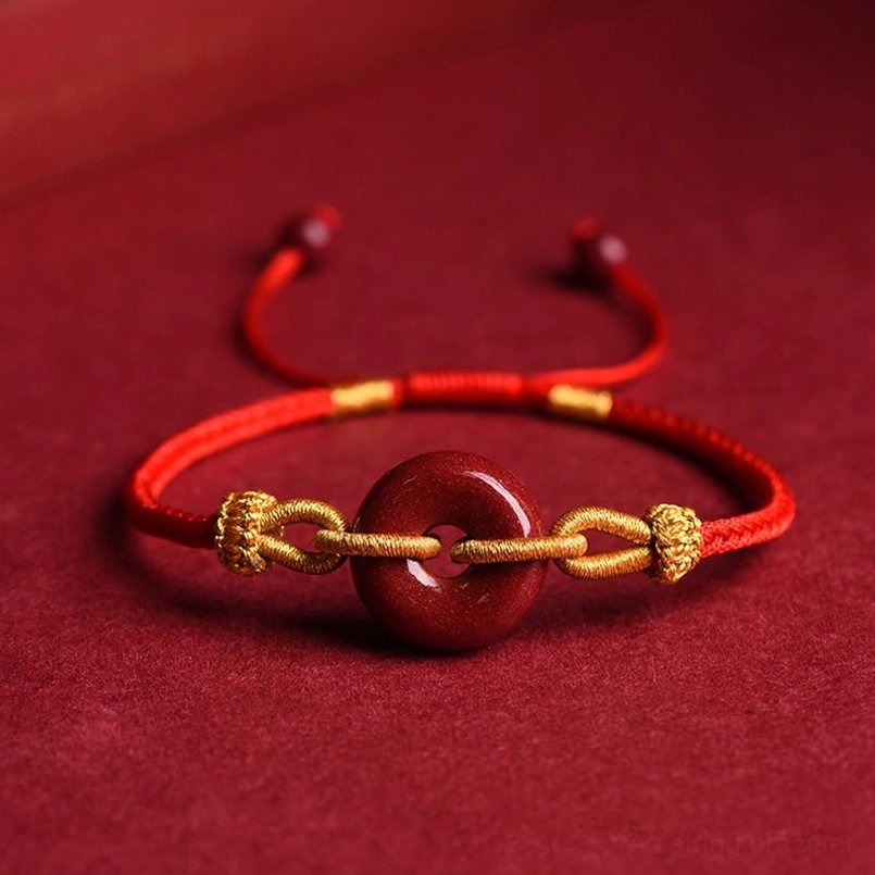 Handmade cinnabar peace buckle red string bracelet with gold knot accents, flat lay view