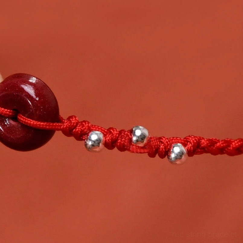 Cinnabar peace buckle macro close-up detail with silver beads and braided red cord