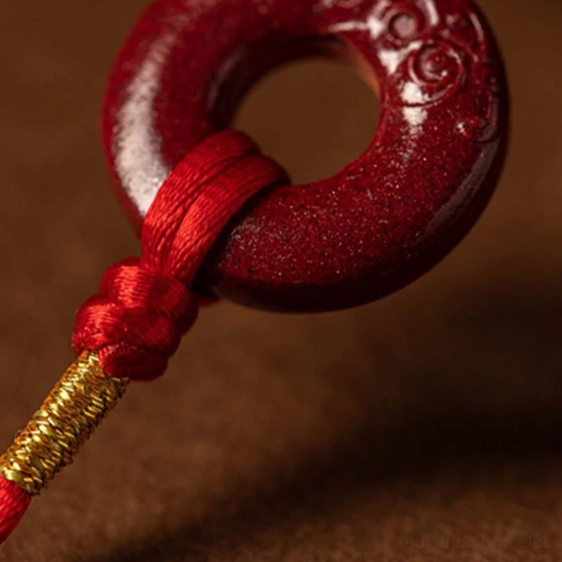 Detailed side view of carved cinnabar peace buckle pendant with red rope and gold thread wrapping