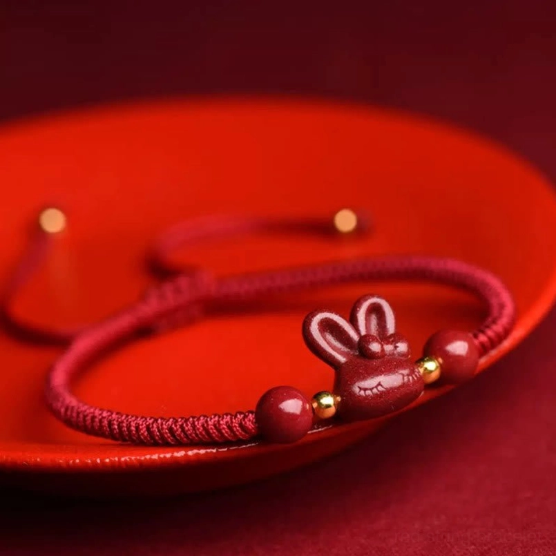 Cinnabar rabbit zodiac bracelet displayed on red ceramic plate, featuring natural stone beads and adjustable pull cord design