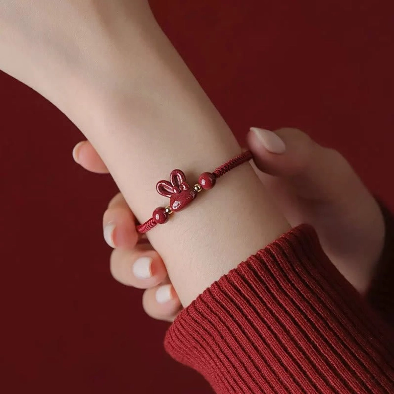 Woman wearing cinnabar rabbit red string bracelet on wrist with burgundy knit sleeve, side view close-up of charm