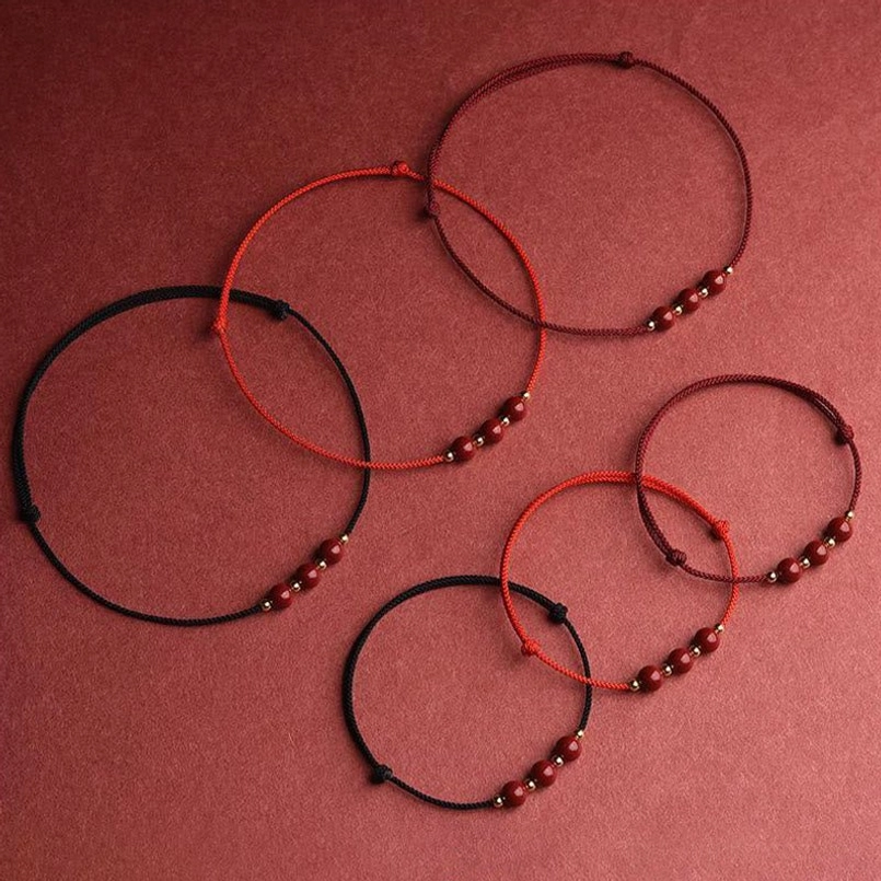 Assorted cinnabar bead bracelets with red and black cord options flat lay on fabric