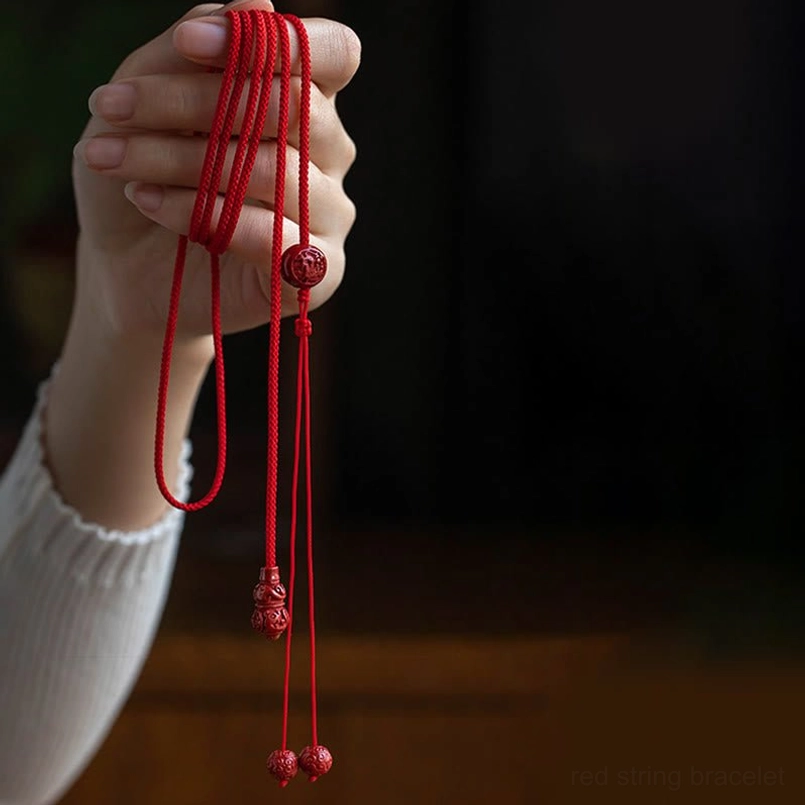 Hand-held view of braided red string belly chain with carved cinnabar zodiac pendants