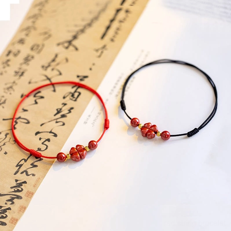 Red and black cinnabar string bracelets with four-leaf clover charm comparison on calligraphy paper