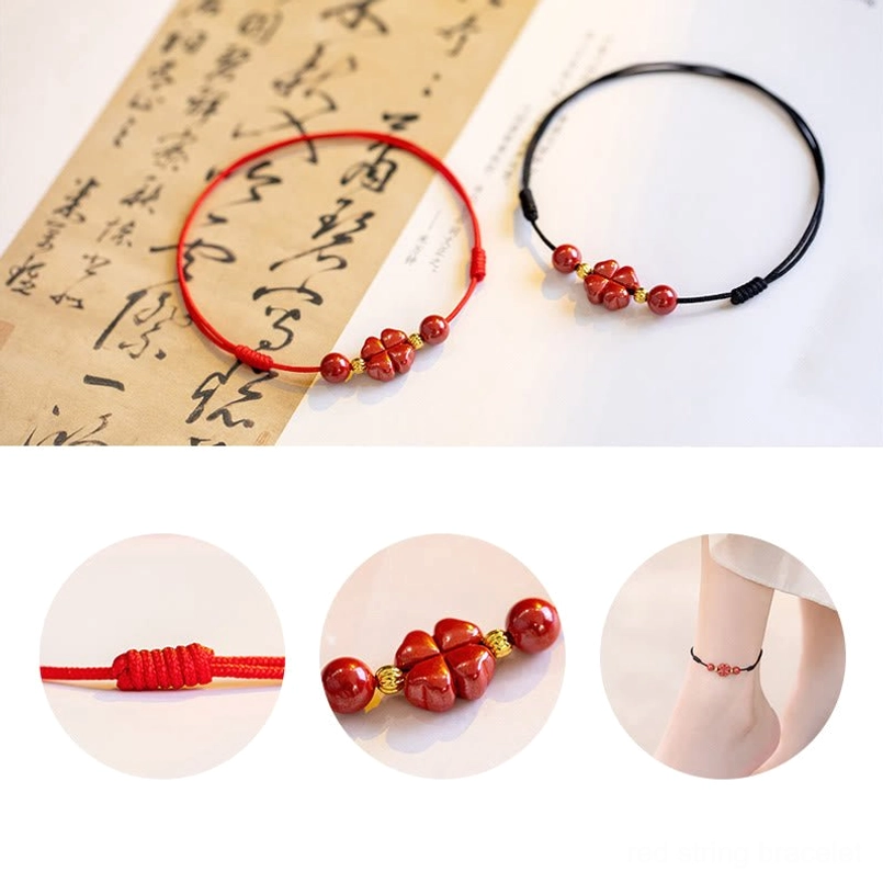 Multiple cinnabar red string bracelets with four-leaf clover charm displayed on calligraphy paper