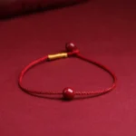 Natural cinnabar red string bracelet with gold bead detail on wine-red background