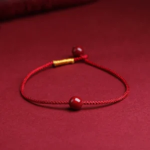 Natural cinnabar red string bracelet with gold bead detail on wine-red background