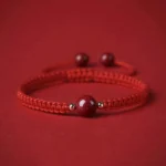 Cinnabar red string bracelet with braided rope and central bead on red fabric background